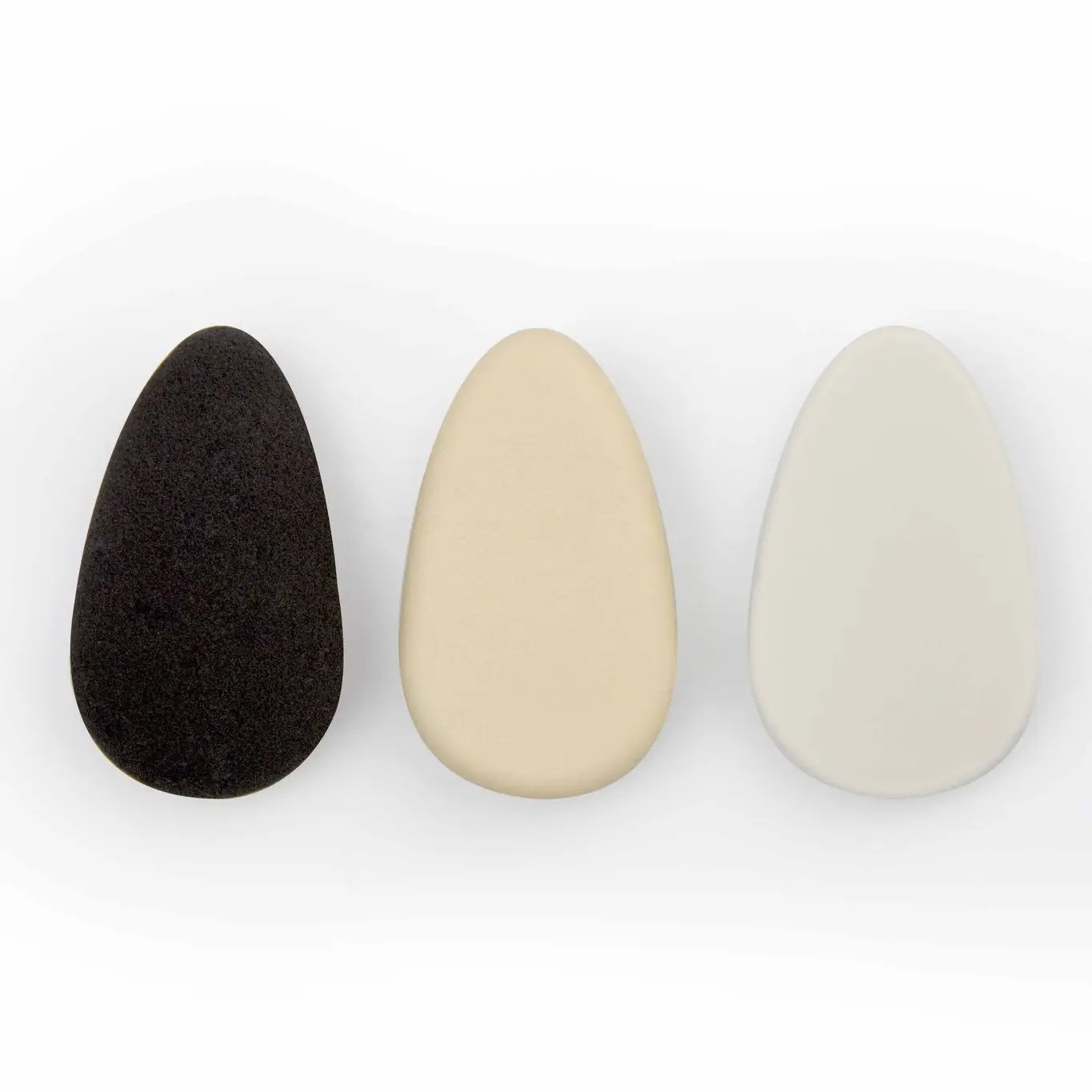 Drei tropfenförmige Make-up-Schwämme in Schwarz, Beige und Weiß auf weißem Hintergrund.