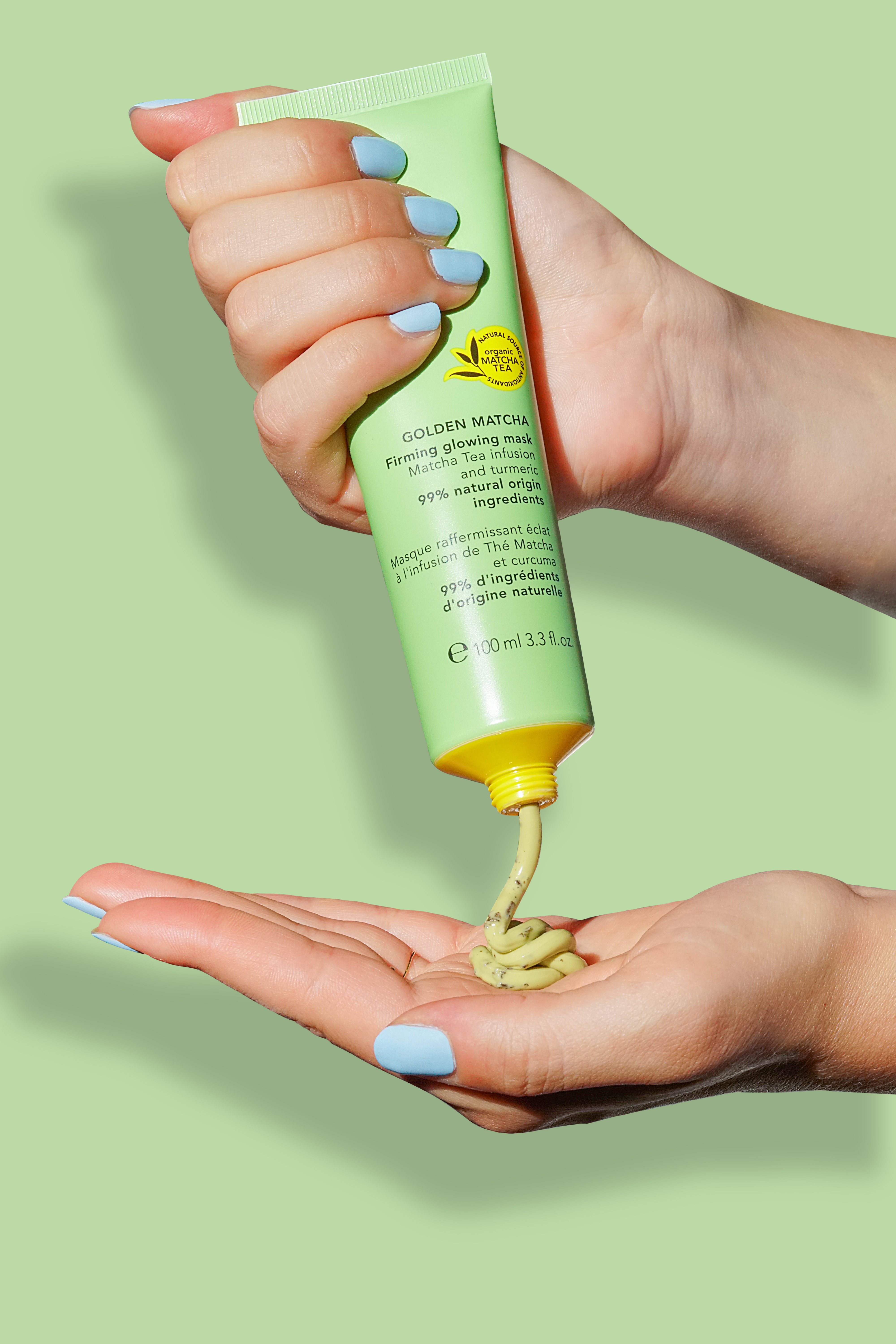 Eine Hand drückt eine grüne Tube mit GOLDEN MATCHA Firming Glowing Mask auf die andere Hand.