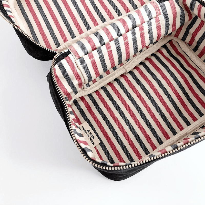 Schwarze Kosmetiktasche mit rot-schwarz-weiß gestreiftem Innenfutter, geöffnet, auf weißem Hintergrund.