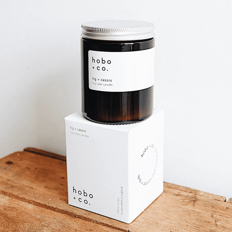 Hobo+Co. Fig & Cassis Duftkerze, 180ml, auf Holzoberfläche, weiße Verpackung, schwarzes Glas.